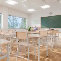 Puste ławki i krzesła w sali lekcyjnej, sugerujące rezygnację ze szkoły. Słońce wpada przez okna, oświetlając drewnianą podłogę.