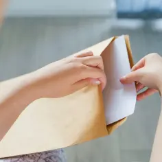Dłonie wkładają białą kartkę do brązowej koperty. Właśnie przygotowuję się, by dowiedzieć się, jak zaadresować list do Anglii.