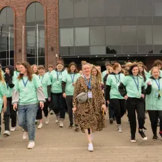 Grupa młodych ludzi w zielonych koszulkach z napisem "Szkoła w Chmurze" idzie przed budynkiem.