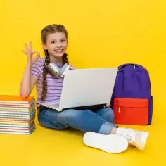 Uśmiechnięta dziewczynka z plecakiem i laptopem pokazuje znak OK. Zastanawia się, ile wynosi subwencja na ucznia, by kupić więcej książek.