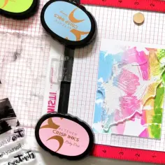 Stempel, tusze i kolorowa kartka z motywem liści na kratkowanym tle.