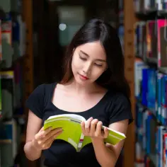 Młoda kobieta w bibliotece czyta książkę. Zastanawia się, od jakiej średniej jest stypendium, by móc kontynuować naukę.