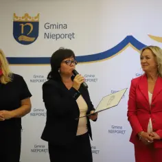 Uzasadnienie wniosku o nagrodę kuratora oświaty: przemawia kobieta z mikrofonem, trzymając dokument. Obok stoją dwie kobiety.