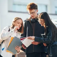 Trzech studentów dyskutuje nad notatkami, ich status ucznia widoczny w zaangażowaniu.