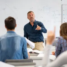 Nauczyciel matematyki wyjaśnia zagadnienia przedmioty w 3 klasie liceum. Uczniowie uważnie słuchają, jeden z nich podnosi rękę.