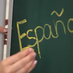 Ręka pisze kredą na tablicy słowo "Español". Może to być początek nauki drugiego języka lub zwolnienie z drugiego języka.