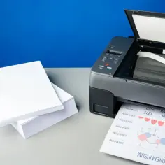 Stos białego papieru obok drukarki atramentowej, gotowy do drukowania. Jaki papier do drukarki atramentowej wybrać, by uzyskać najlepsze rezultaty?