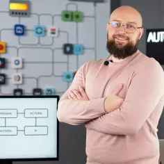 Uśmiechnięty mężczyzna z brodą, w różowym swetrze, prezentuje schemat automatyzacji i AI. To idealne miejsce na edukację domową online.