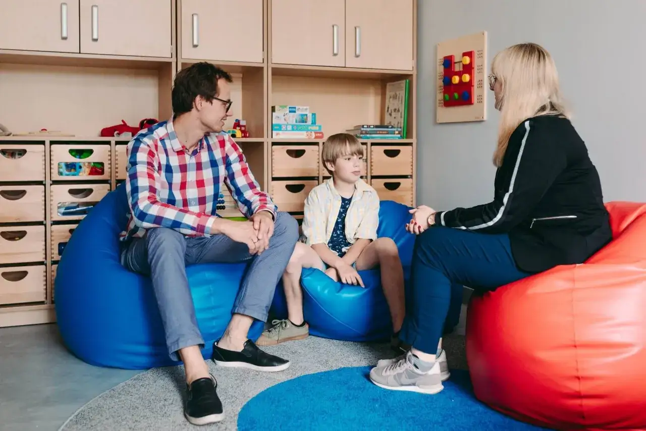 Ojciec, syn i psycholog szkolny rozmawiają w przytulnym pokoju.