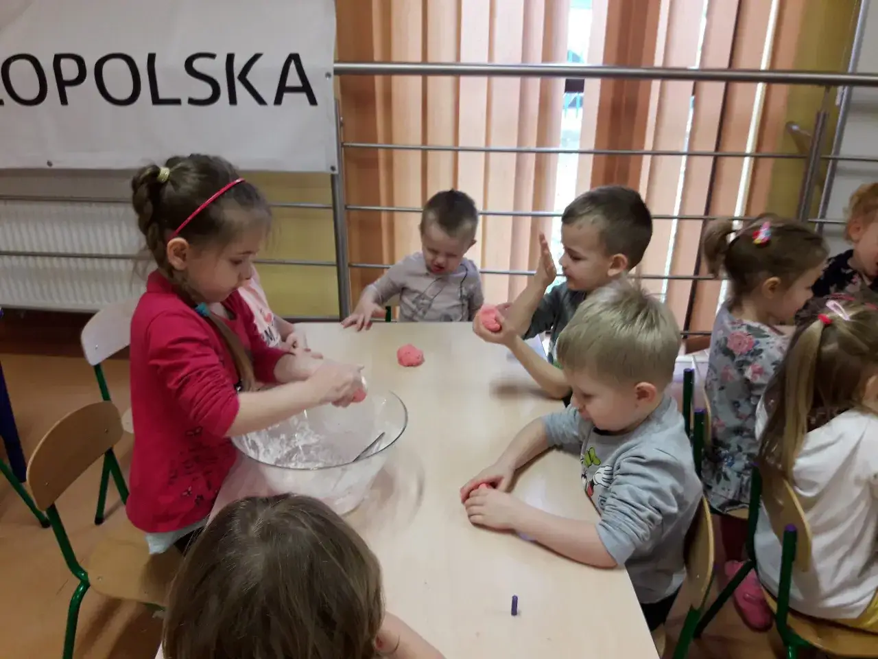 Dzieci lepią z różowej masy, która wygląda jak papier mâché.