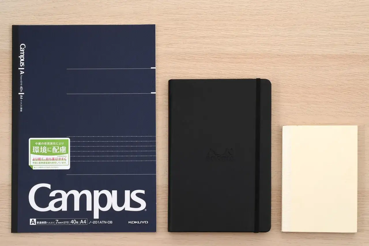 Trzy zeszyty: granatowy Campus A4, czarny Rhodia i kremowy MD Paper. Zeszyt Campus ma wymiary b5.